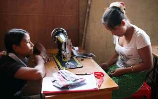 A trainer looks across a sewing machine as her student works hard. The young woman is taking part in a pilot project run by UNHCR in Kachin state to foster cohesion among internally displaced women. © UNHCR/M.Savary