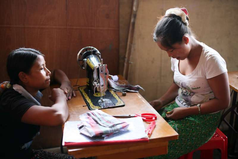 A trainer looks across a sewing machine as her student works hard. The young woman is taking part in a pilot project run by UNHCR in Kachin state to foster cohesion among internally displaced women. © UNHCR/M.Savary