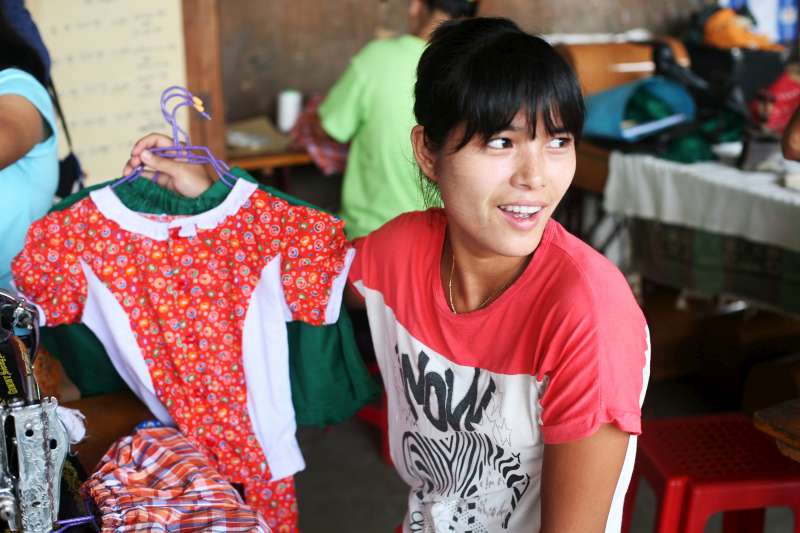 One of the tailoring trainees proudly holds up children's clothing that she has made. © UNHCR/M.Savary