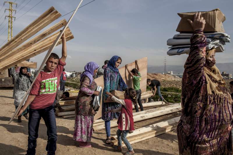 Syrian refugees at an informal settlement in Lebanon carry aid items, including wood to strengthen their shelters for winter.