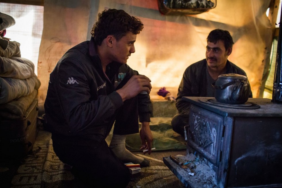 Two of Hala's brothers – Nemer, 17, and Kamel, 18 – keep warm by the stove inside their shelter in Lebanon's Bekaa Valley. 