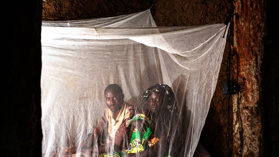 Innocent and Immaculate sit with their youngest child beneath a mosquito net in Nakivale refugee settlement.