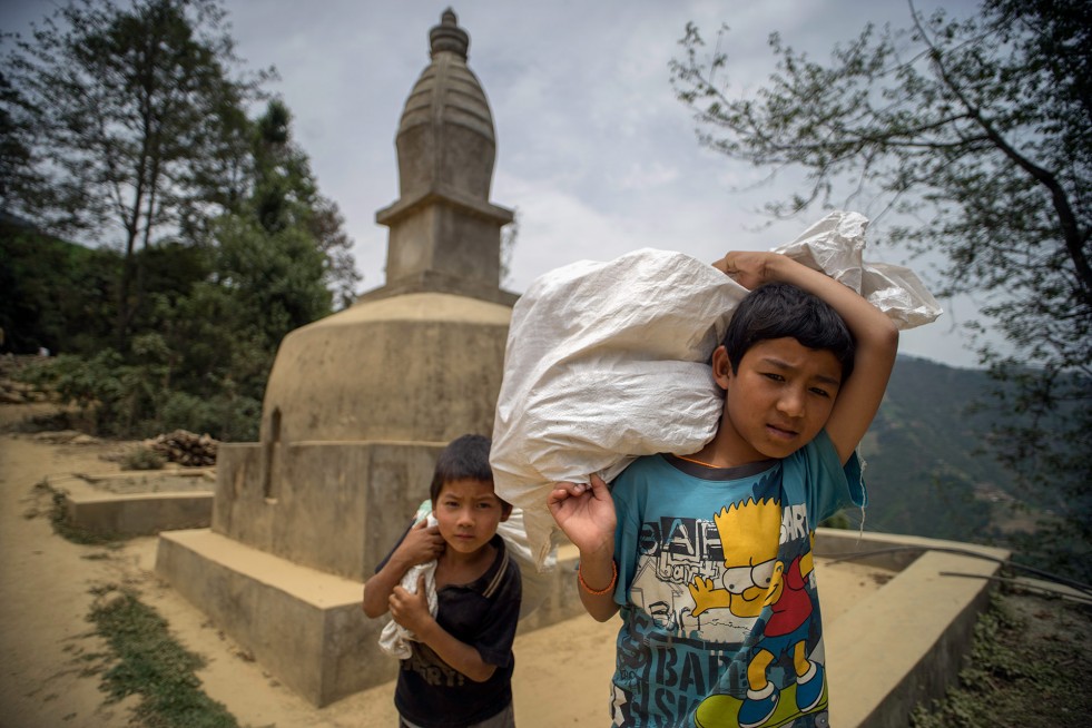 Sarod Tamang, 12, and Ramesh Ghalan, 7, carry tarps and other relief supplies past a Buddhist chorten, or stupa, following a distribution in Jhankridanda village, in Lalitpur District, Nepal.