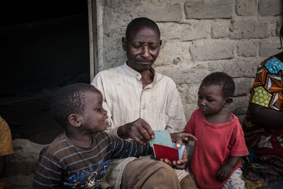 Flanked by two of his children, Venant Kabura holds his identity card in the Congolese village of Majengo, where his family found shelter after fleeing political violence in Burundi.