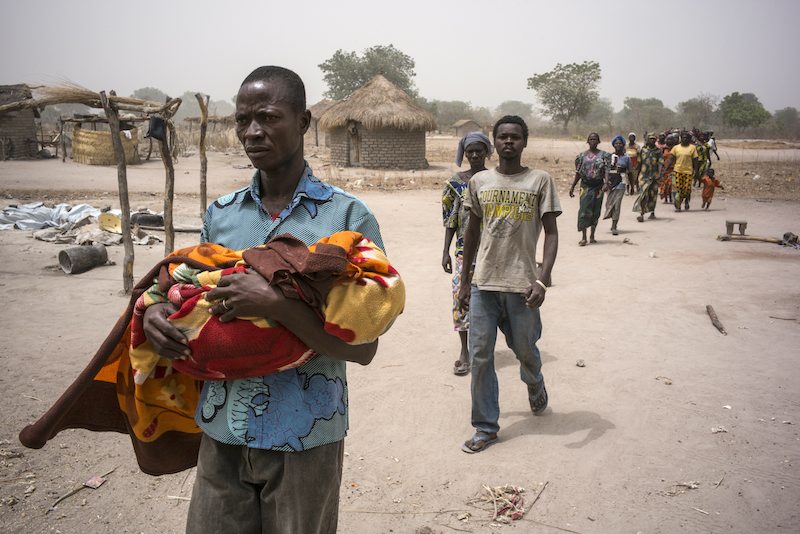 Followed by villagers and fellow refugees from the Central African Republic, a grieving father carries the body of his eight-year-old daughter, who died of unknown causes. 