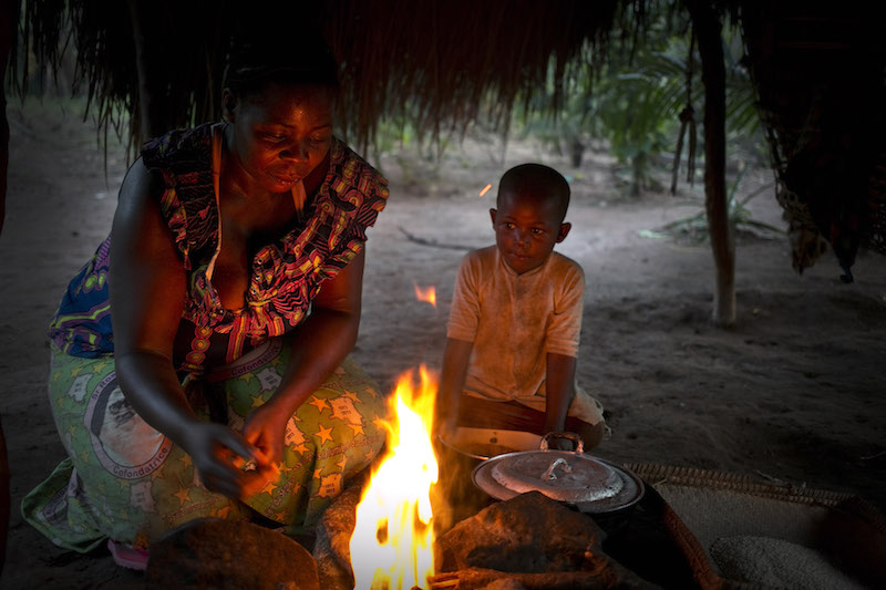 As one of her young sons looks on, Pascaline lights a fire so she can cook an evening meal for her family in their home in Dungu.