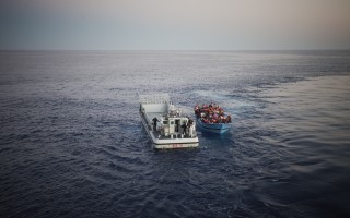 An Italian Navy rescue vessel, called the GIS, pulls up next to the first boat in order to transfer its desperate occupants. The GIS will then drive into the belly of the much larger San Giorgio, where people can safely disembark.