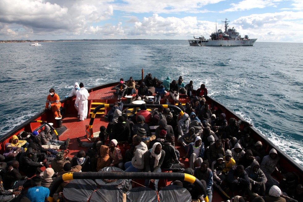 Refugees and migrants wait to disembark from an Italian Navy Ship onto a tugboat that will take them to Pozzallo. 