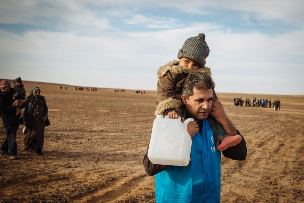 A UNHCR staff member carries a young Syrian refugee toward the safety of the Jordanian border as he approaches the end of a long and dangerous journey. © UNHCR / J. Kohler