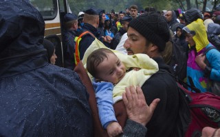 A father cradling his sick child waits in the rain to board a bus to a police pre-registration centre in Hungary.