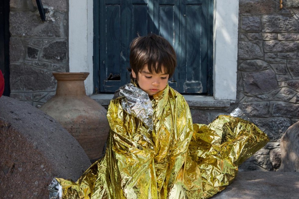 A young refugee boy from Afghanistan warms up with an emergency blanket after crossing from Turkey to the Greek island of Lesvos in an inflatable boat. 