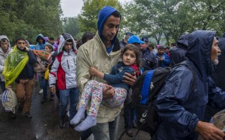 Refugee family groups, in the rain at a collection point close to the Serbian border, wait to board buses to go to the registration centre run by the Hungarian authorities.