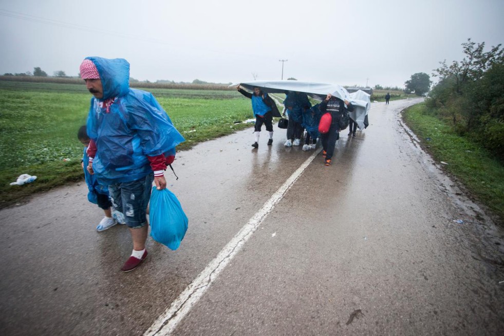 A group of refugees use UNHCR tents to protect themselves from the rain as they arrive in Bapska, Croatia.