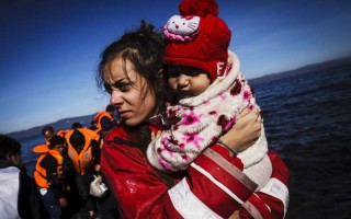 Sur l'île grecque de Lesbos, une volontaire tient une petite fille dans ses bras, peu après l'arrivée de sa famille à bord d'un bateau pneumatique.