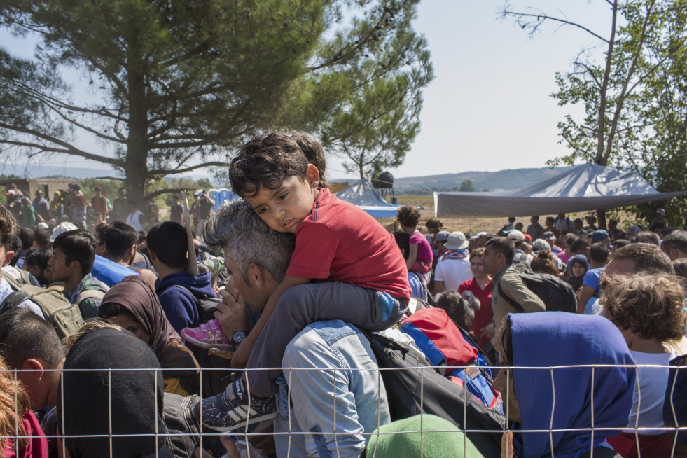A young Afghan refugee sits on his fathers shoulders in the scorching mid-day sun.