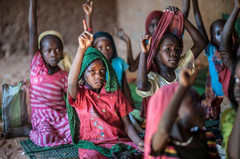 Child refugee Zoera, in faded red dress with green headscarf, attends class at Djabal camp in Chad.