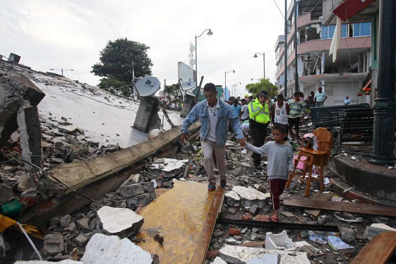 People walk among the debris of a collapsed building in the town of Pedernales, Ecuador, following a 7.8 magnitude earthquake