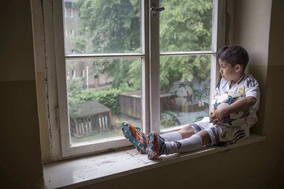 Seven-year-old refugee Ahmad Alzaher gazes out the window of the Potsdam apartment he shares with his family. He escaped war in Syria and dreams of becoming an international football star. © UNHCR/Daniel Morgan