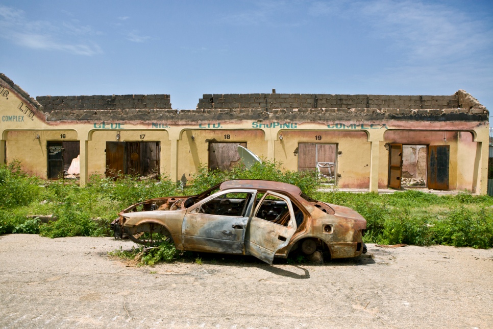 Une voiture réduite en cendres immobilisée dans une rue bordée de maisons détruites de Gwoza, au Nigéria, récemment libérée par les forces armées nigérianes. © HCR/Hélène Caux