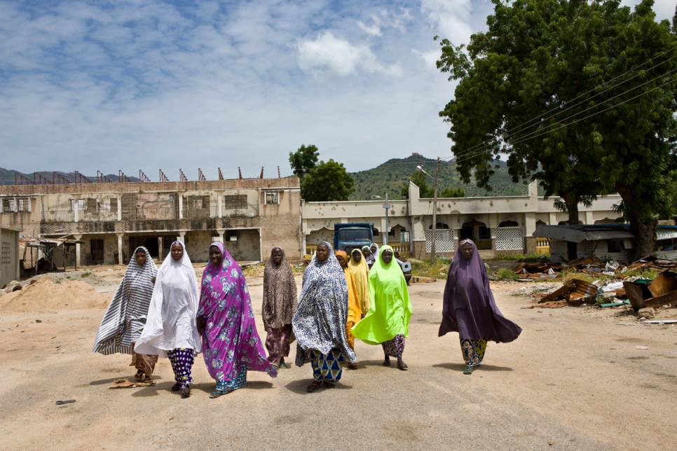 Un groupe de femmes marche dans la rue devant les ruines de l’ancien palace de l’Emir bombardé à Gwoza, au Nigéria. © HCR/Hélène Caux