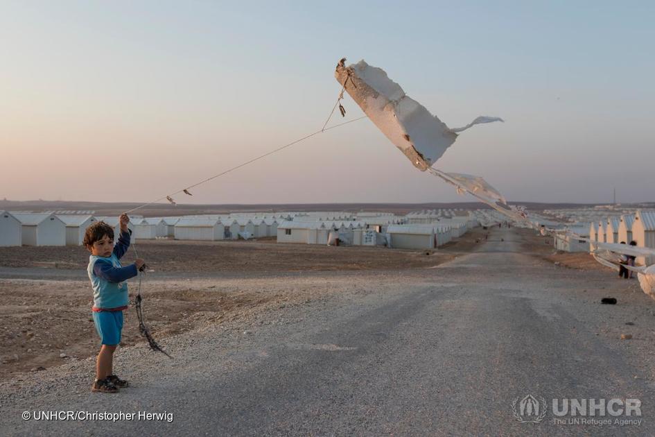 Jordan. Evening view over Azraq Camp. Young Syrian refugee boy flies a homemade kite made from a piece of insulation