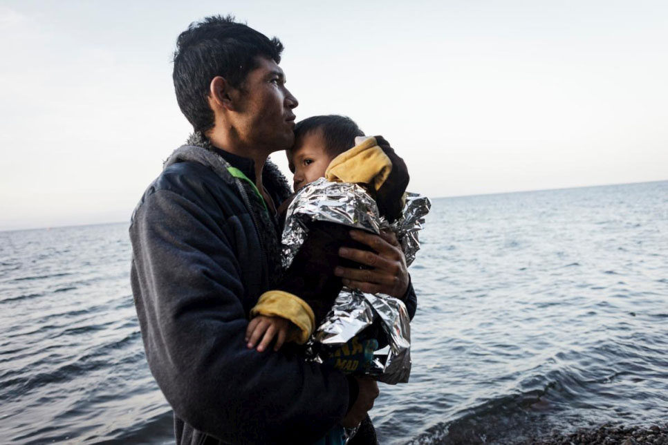 A young refugee from Afghanistan holds his young son and looks at the sea after reaching safely the shores of Lesbos island, having crossed the Aegean sea from Turkey in an inflatable boat full of Afghan refugees. © UNHCR/Achilleas Zavallis