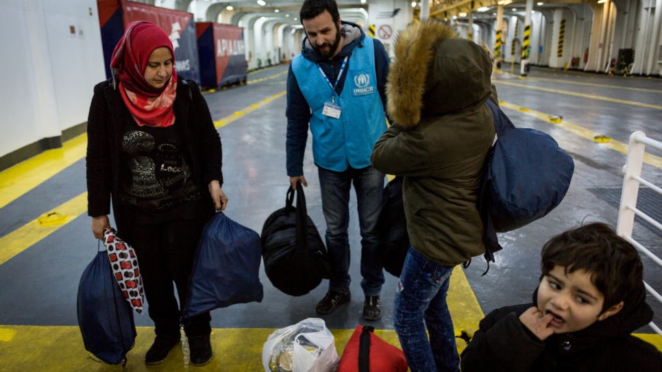 A UNHCR staff member helps Falak and her sons carry their bags onto a ferry bound for Athens. © UNHCR/Achilleas Zavallis