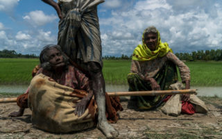 Rohingya refugee Mabia Khatun, 75, (left) rests after being carried to Bangladesh from Myanmar in a blanket on a bamboo pole as Amina Khatun, 80, her sister in law (right) sits nearby. © UNHCR/Adam Dean
