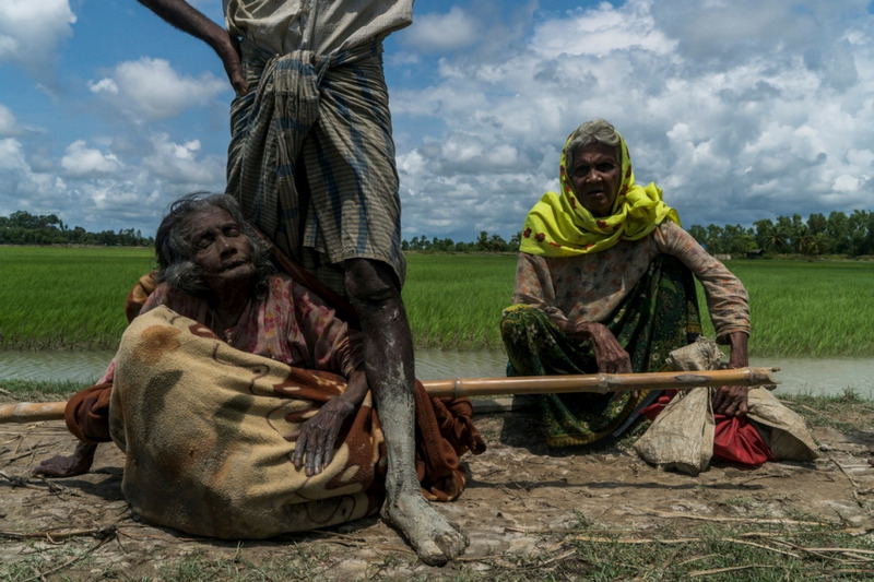 Rohingya refugee Mabia Khatun, 75, (left) rests after being carried to Bangladesh from Myanmar in a blanket on a bamboo pole as Amina Khatun, 80, her sister in law (right) sits nearby. © UNHCR/Adam Dean