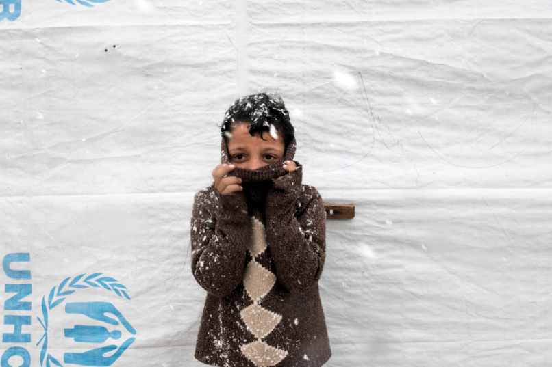 A young Syrian refugee boy, Omar (11 years old) standing outside a tent covering his face to avoid the cold in Bekaa, Lebanon.