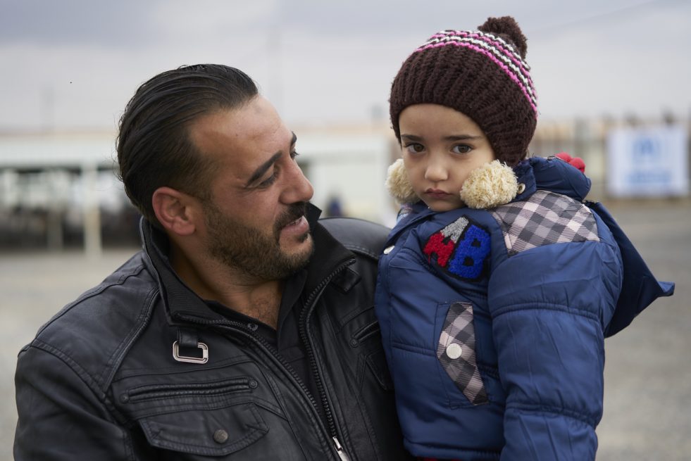 Syrian refugee Marseel, 30, carries his daughter Yaucot, 5, as they wait outside the new arrivals distribution point in Azraq refugee camp, Zarqa Governorate, Jordan. ; As of 15 November 2017, Jordan hosts 655,056 registered Syrian refugees, of which 53,229 are registered in Azraq camp.
