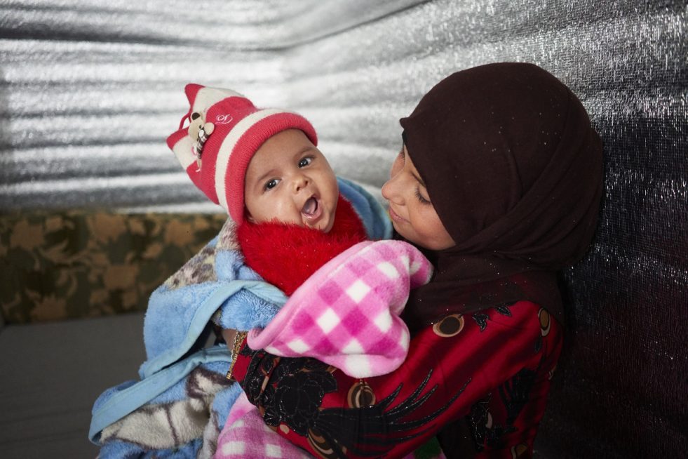 Syrian refugee Alaa, 11, holds her two-month-old infant sister Muna at their shelter in Azraq refugee camp, Zarqa Governorate, Jordan. The family received winterization assistance from UNHCR in the form of insulation material and a gas heater. © UNHCR/David Azia