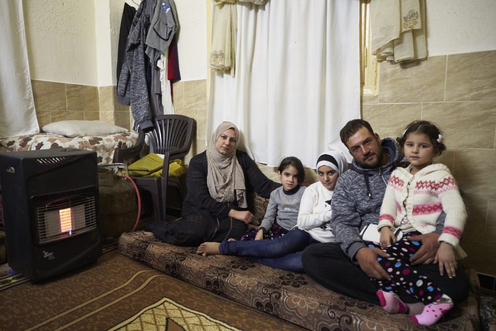 From left, Syrian refugee Um 33, her daughters Maha, 8, Jodi, 12, husband Abu , 35, and daughter Jana, 5, sit in the only heated room of the home they rent in Zarqa, Zarqa Governorate, Jordan. 