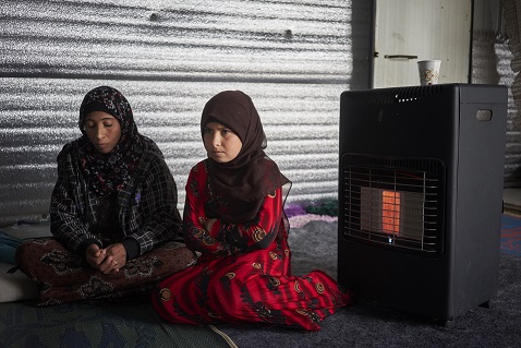 Syrian refugee Alaa, 11, right, and her mother Wardah sit next to their gas heater in their shelter in Azraq refugee camp, Zarqa Governorate, Jordan. The family received winterization from UNHCR assistance in the form of insulation material and a gas heater. © UNHCR/David Azia