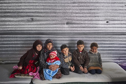 (From left) Syrian refugee Alaa, 11, her mother Wardah, two-month-old infant sister Muna, brothers Abdallah, 9, Abd Alrahman, 7, and sister Rajaa, 5, sit in their shelter in Azraq refugee camp, Zarqa Governorate, Jordan. The family received winterization assistance from UNHCR in the form of insulation material and a gas heater. © UNHCR/David Azia