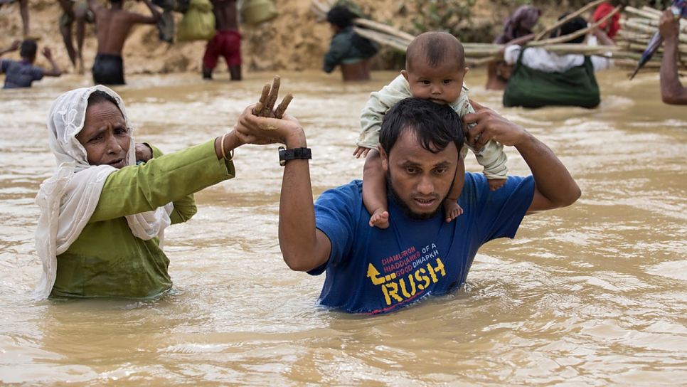 A family of Rohingya refugees from Myanmar crosses a river swollen by monsoon rains at Kutupalong, Bangladesh, during the 2017 monsoon season. © UNHCR/Paula Bronstein