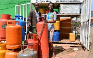 A man and a woman standing behind a red gas tank in front of a store