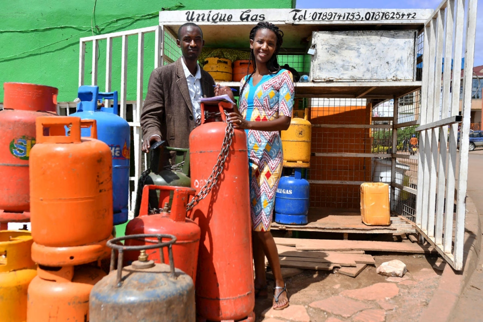 A man and a woman standing behind a red gas tank in front of a store