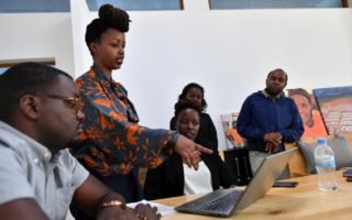 Rwanda, a lady points at a laptop on table directing surrounding people to attention