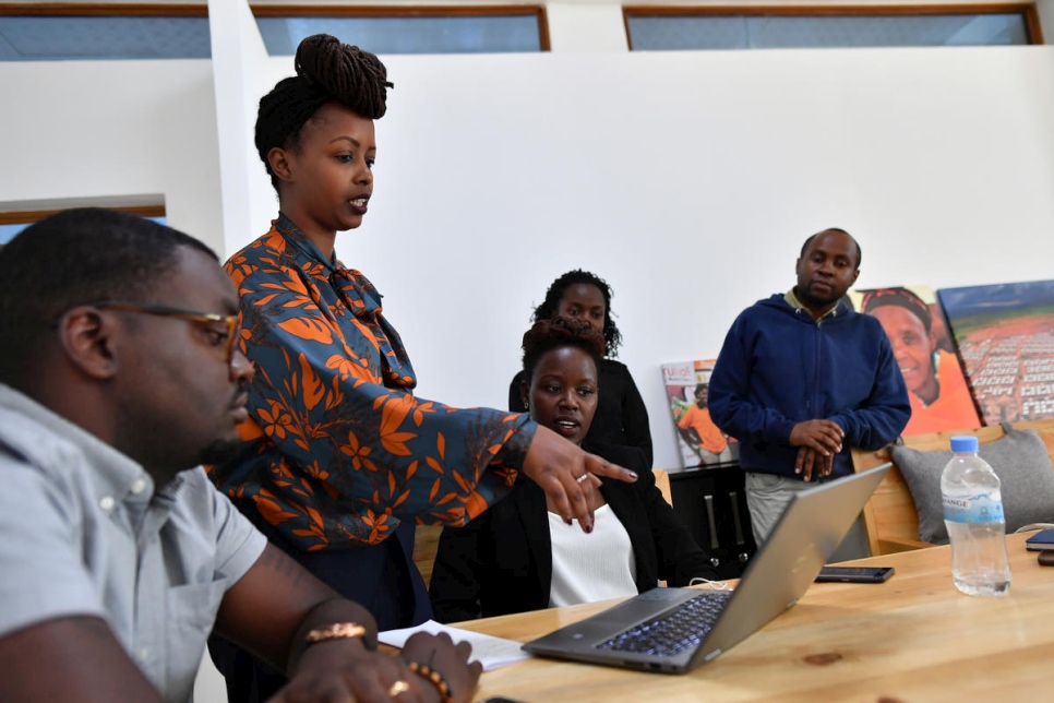 Rwanda, a lady points at a laptop on table directing surrounding people to attention