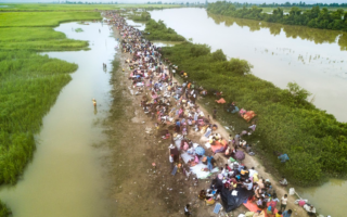 refugees walking along a river bank stepping in solidarity with one another