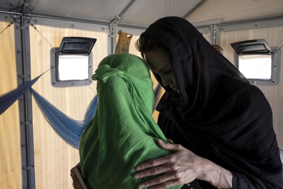 Two ladies in head scarves are standing face to face and providing each other support