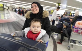 a woman wearing a black hijab pushes a baggage cart with her baby sitting in the cart, they are beside a luggage carousel at an airport