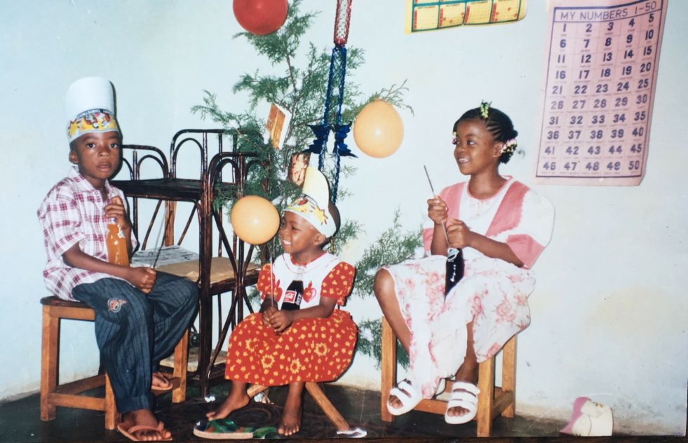 Three children sitting on chairs with a plant behind them and balloons around them celebrating a birthday