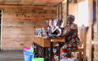 Five woman stitting in a row in front of a brightly lit window making soap