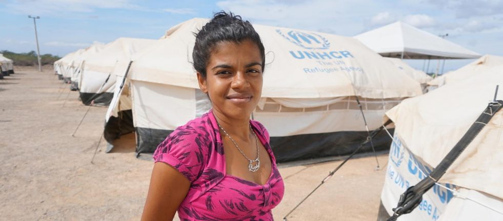 Venezuelan lady smiles for a photo posing in front of a row of UNHCR branded refugee tents