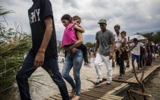 A group of Venezuelans walk across a makeshift bridge over a river