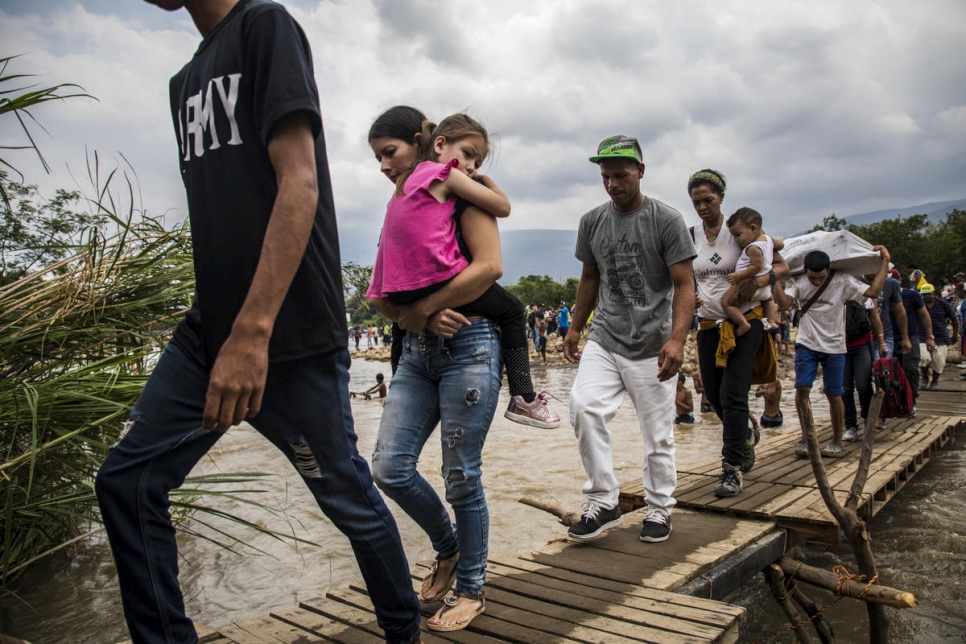A group of Venezuelans walk across a makeshift bridge over a river