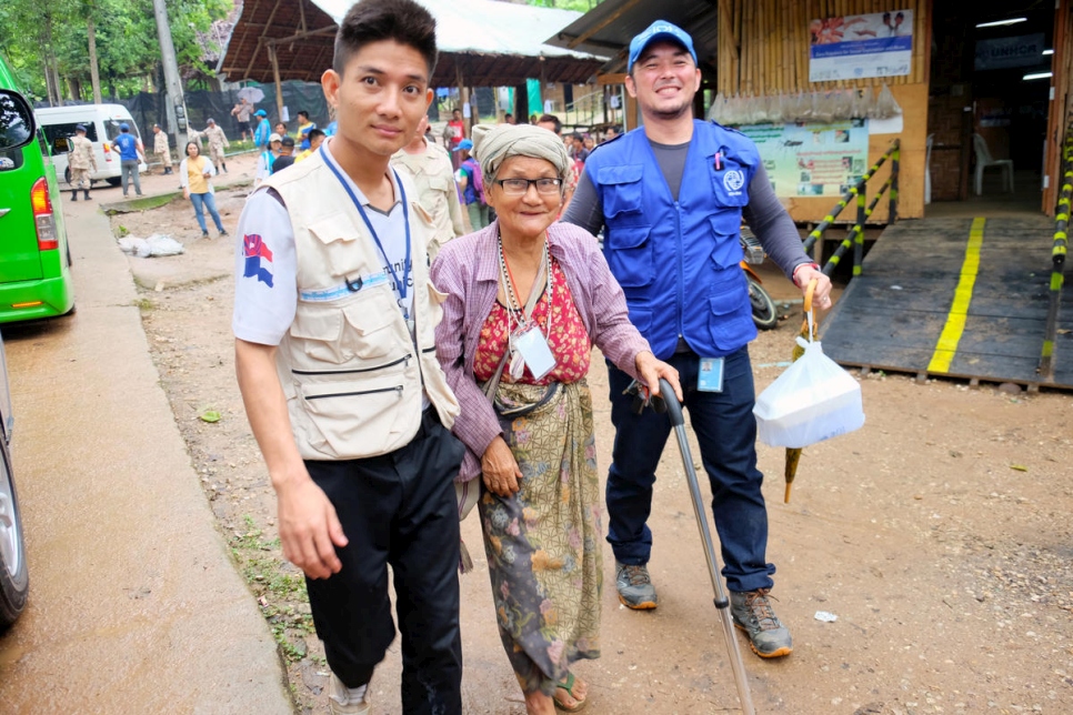 An elderly refugee is being helped to walk down the street by two young humanitarian men