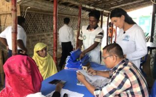 Two Rohingya women in head scarves sit at a table getting identification documents from a man sitting across from them